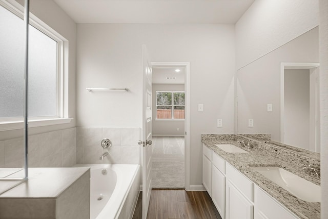 bathroom featuring double vanity, wood finished floors, a bath, and a sink