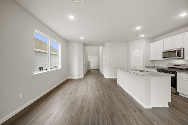 kitchen with dark wood-type flooring, a center island with sink, a sink, appliances with stainless steel finishes, and baseboards