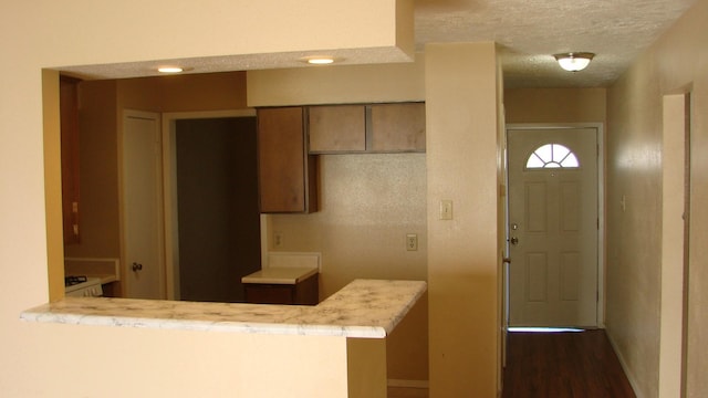 kitchen with a peninsula, a textured ceiling, light countertops, and dark wood-type flooring