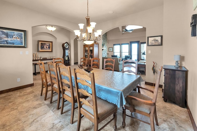 dining space with arched walkways, ceiling fan with notable chandelier, and baseboards