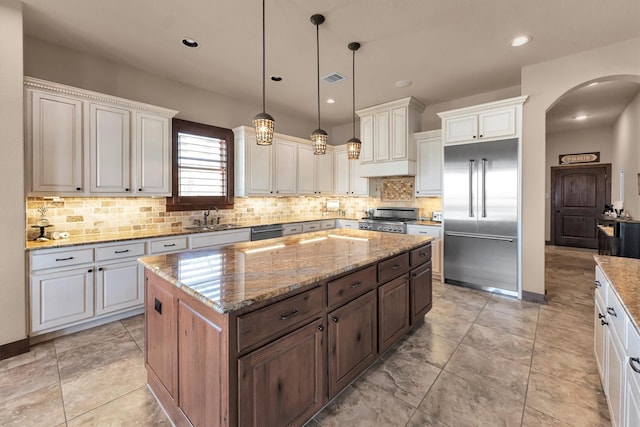 kitchen featuring visible vents, a sink, light stone counters, a kitchen island, and stainless steel appliances