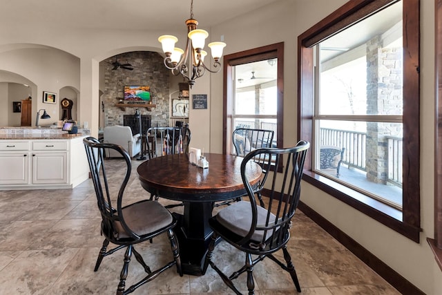 dining space featuring a stone fireplace, a notable chandelier, and baseboards