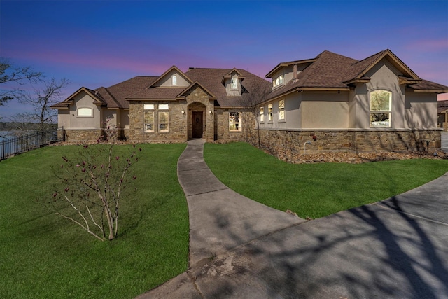 french country style house with stucco siding, stone siding, a lawn, and fence