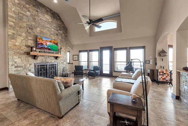 living area featuring a stone fireplace, high vaulted ceiling, arched walkways, and ceiling fan