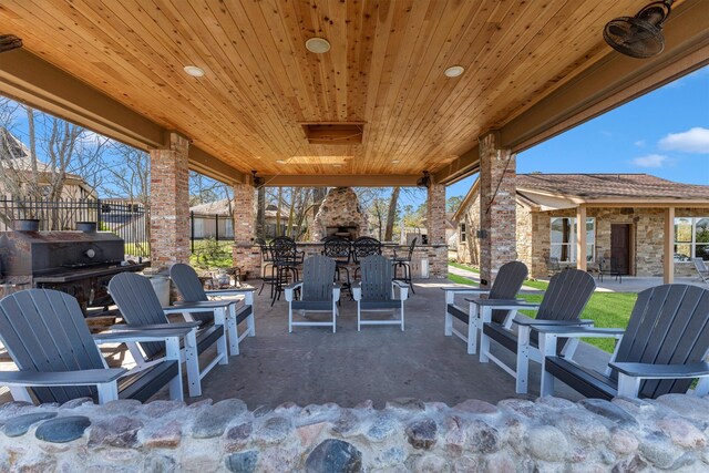 view of patio featuring outdoor dry bar, a grill, a fireplace, and fence