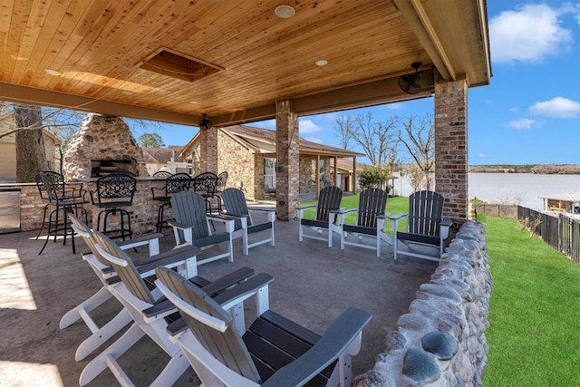 view of patio with fence, a water view, outdoor dry bar, and a large fireplace