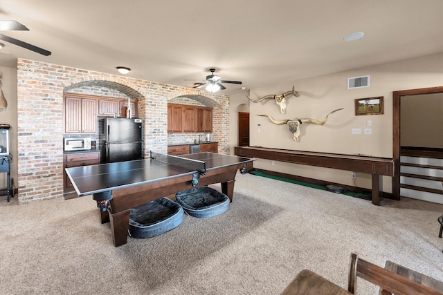 playroom with visible vents, brick wall, carpet flooring, arched walkways, and a ceiling fan