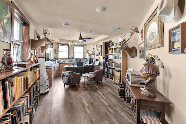 living area featuring visible vents, a textured ceiling, a tray ceiling, and wood finished floors