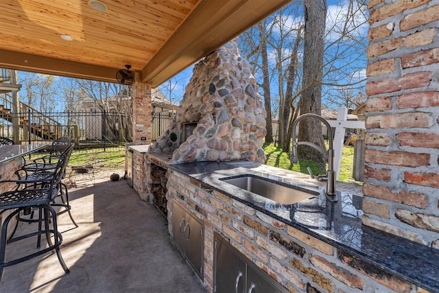 view of patio / terrace with an outdoor stone fireplace, fence, and a sink