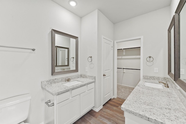 bathroom featuring wood finished floors, toilet, two vanities, and a sink