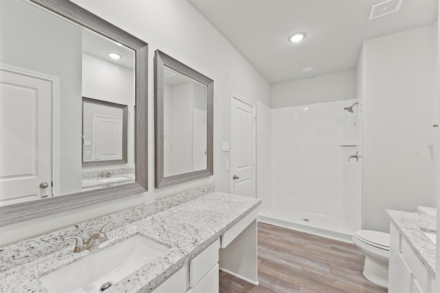 full bath featuring vanity, wood finished floors, visible vents, tiled shower, and toilet