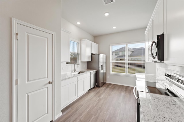 kitchen featuring light wood finished floors, a sink, white cabinets, appliances with stainless steel finishes, and tasteful backsplash