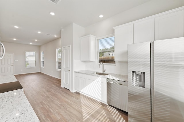 kitchen with a sink, light stone countertops, appliances with stainless steel finishes, and white cabinets