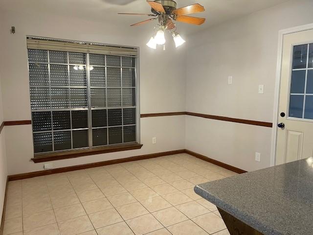 interior space with baseboards, light tile patterned flooring, and a ceiling fan