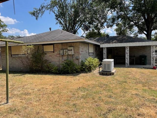 back of house featuring central air condition unit, stone siding, a lawn, and brick siding