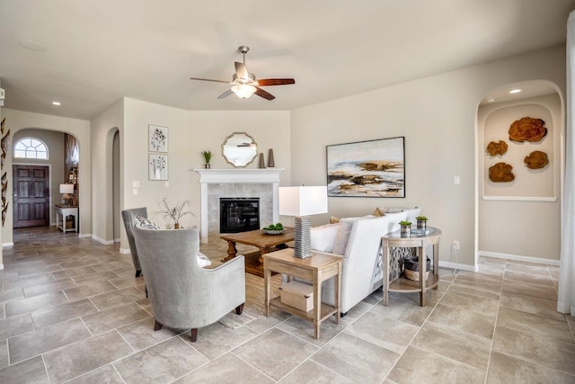 living room featuring arched walkways, a tiled fireplace, baseboards, and a ceiling fan