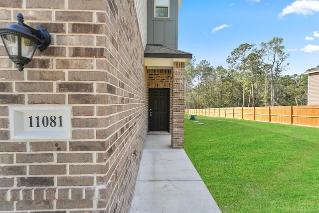 doorway to property featuring brick siding, a lawn, board and batten siding, and fence