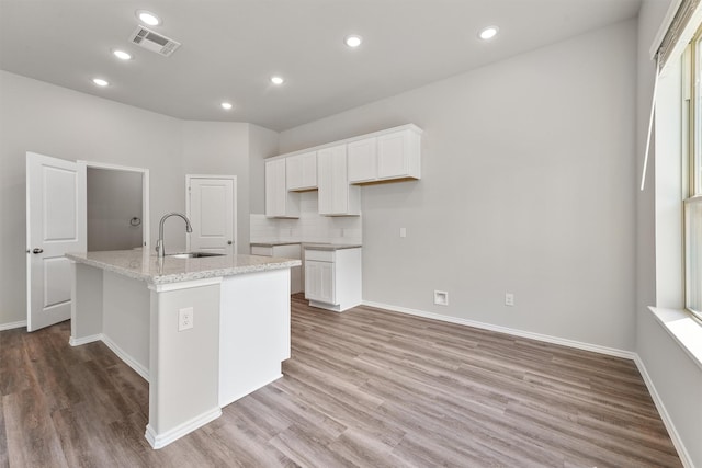 kitchen featuring visible vents, light wood-style flooring, an island with sink, a sink, and white cabinetry