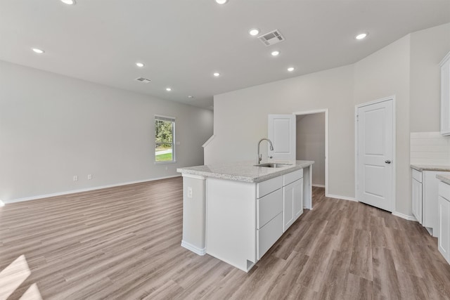 kitchen with visible vents, white cabinets, light wood-type flooring, and a sink