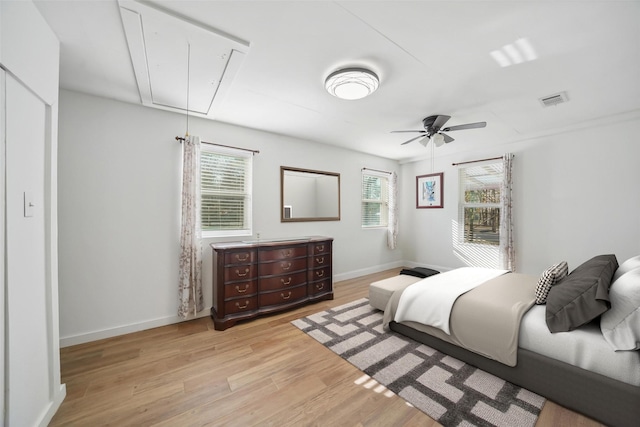 bedroom with light wood-type flooring, visible vents, baseboards, attic access, and ceiling fan