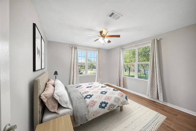 bedroom with visible vents, a ceiling fan, baseboards, and wood finished floors