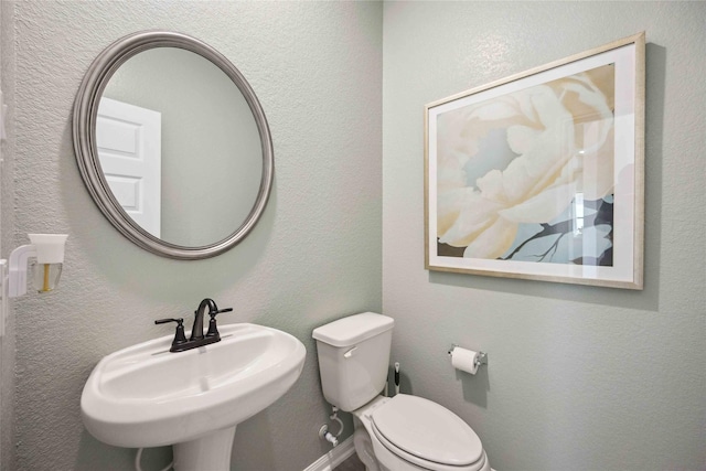 bathroom featuring toilet, a textured wall, baseboards, and a sink