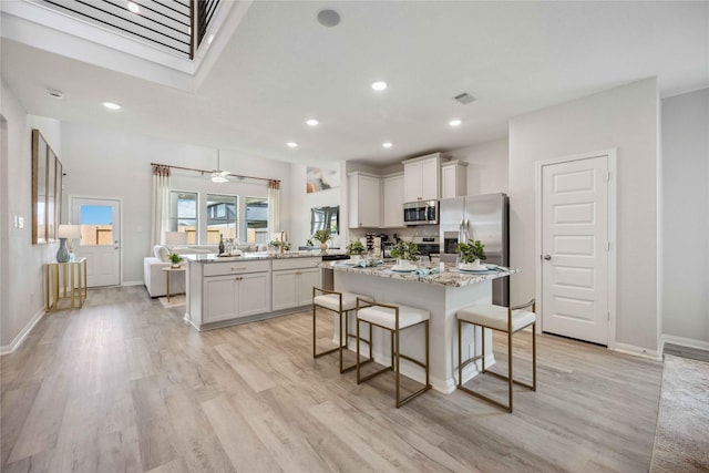 kitchen with a kitchen island, a breakfast bar, a peninsula, light wood-style flooring, and appliances with stainless steel finishes