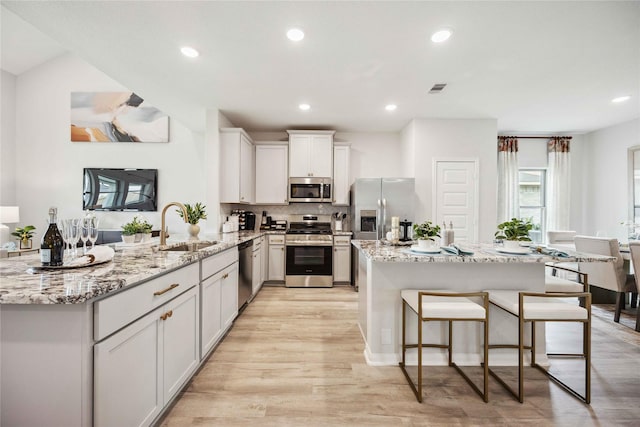 kitchen with light stone countertops, light wood finished floors, a breakfast bar, a sink, and stainless steel appliances