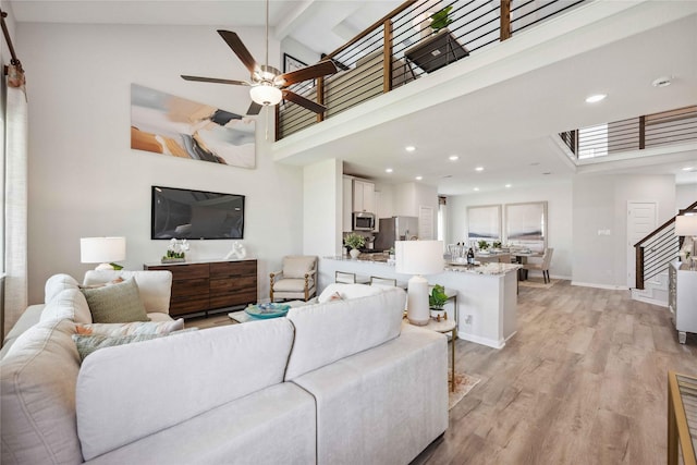 living area with stairway, baseboards, high vaulted ceiling, beam ceiling, and light wood-style floors