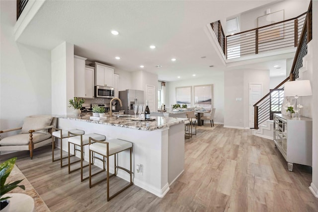 kitchen with light stone counters, light wood finished floors, a peninsula, appliances with stainless steel finishes, and a kitchen breakfast bar