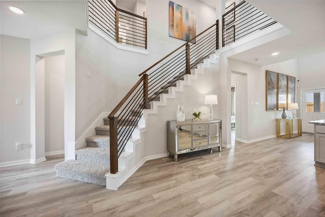 staircase featuring recessed lighting, a high ceiling, baseboards, and wood finished floors