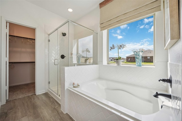 bathroom featuring a spacious closet, a shower stall, a bath, and wood finished floors