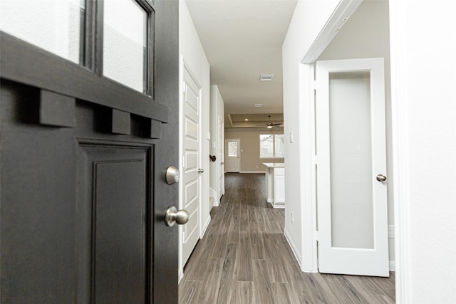 hall featuring visible vents, wood finished floors, and baseboards