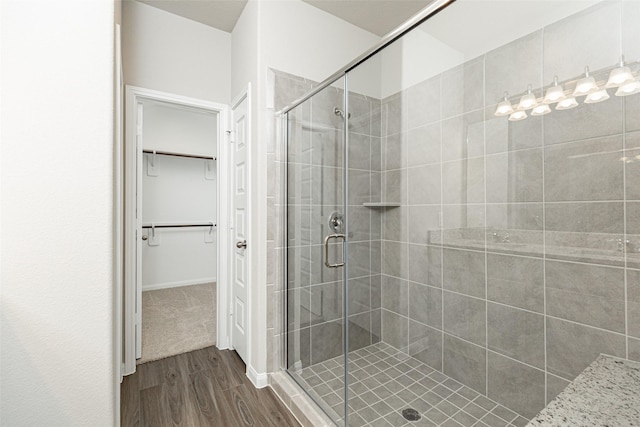 bathroom featuring a walk in closet, wood finished floors, and a stall shower