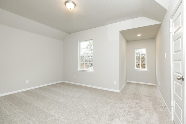 unfurnished room featuring vaulted ceiling, light colored carpet, baseboards, and a wealth of natural light