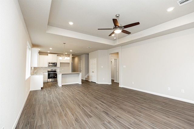 unfurnished living room featuring a tray ceiling, baseboards, visible vents, and wood finished floors