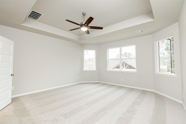 spare room with a tray ceiling, baseboards, visible vents, and light carpet