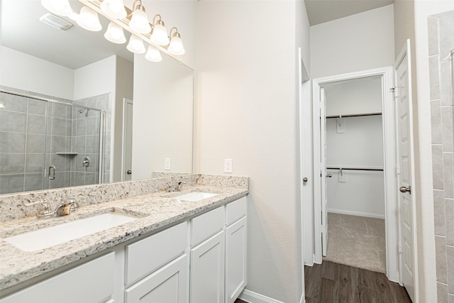 full bath with a spacious closet, wood finished floors, a stall shower, and a sink