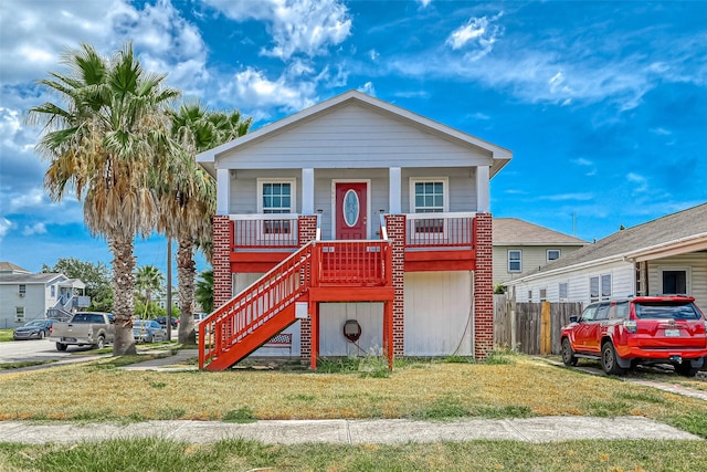 raised beach house with covered porch, stairs, and a front lawn