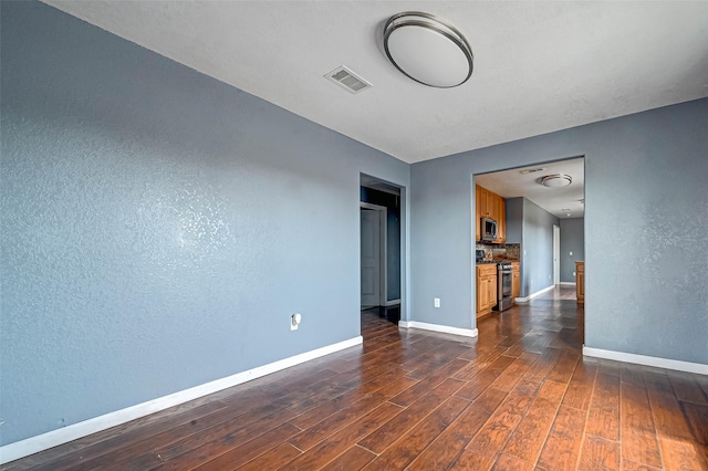 spare room with visible vents, dark wood-type flooring, baseboards, and a textured wall