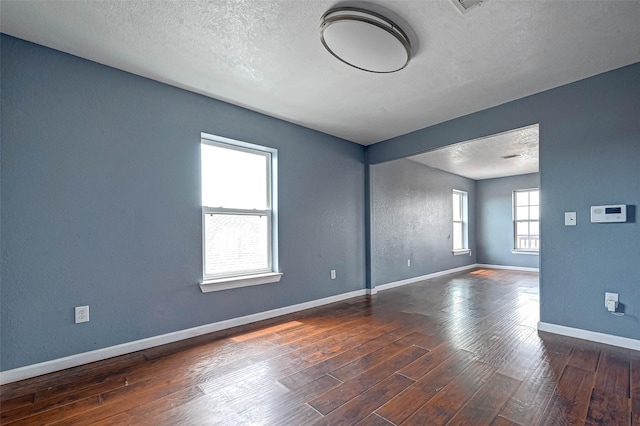 spare room featuring baseboards, a textured ceiling, wood finished floors, and a textured wall