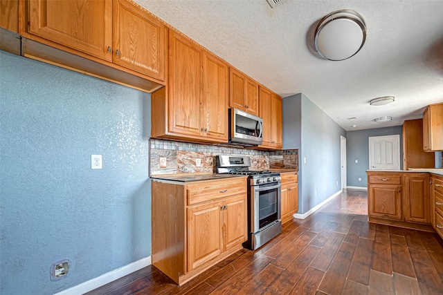 kitchen featuring dark wood-style floors, baseboards, decorative backsplash, appliances with stainless steel finishes, and brown cabinets