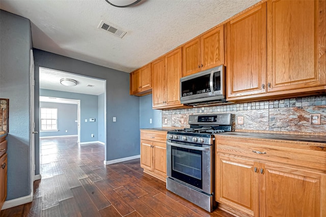 kitchen with dark wood-style floors, visible vents, baseboards, appliances with stainless steel finishes, and backsplash