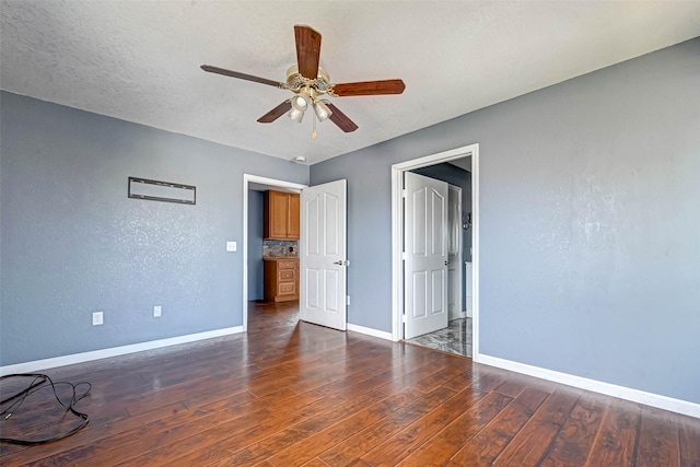 spare room featuring ceiling fan, baseboards, dark wood finished floors, a textured wall, and a textured ceiling