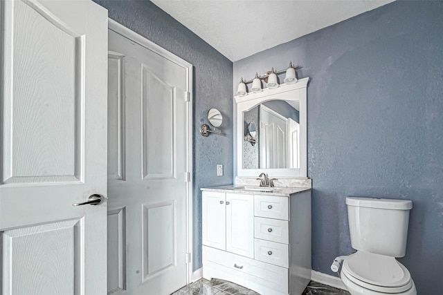 bathroom with vanity, baseboards, toilet, a textured wall, and marble finish floor