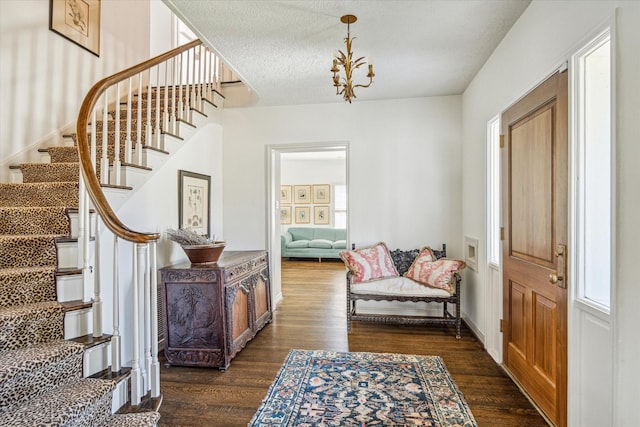 entryway featuring a notable chandelier, a textured ceiling, stairs, and dark wood-type flooring