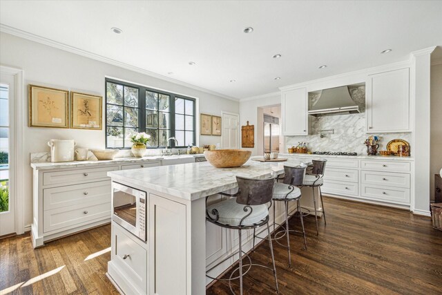 kitchen with stainless steel microwave, a center island, dark wood-type flooring, wall chimney range hood, and decorative backsplash