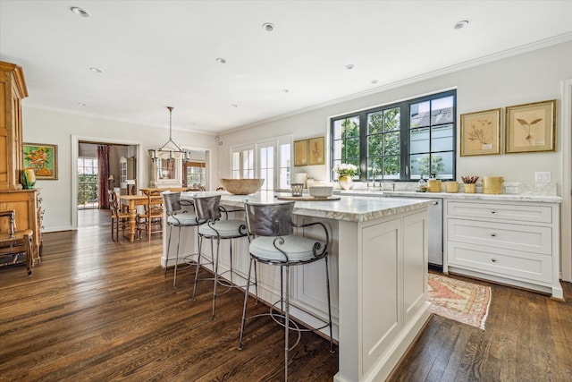 kitchen with dark wood-style flooring, a kitchen bar, crown molding, stainless steel dishwasher, and a center island