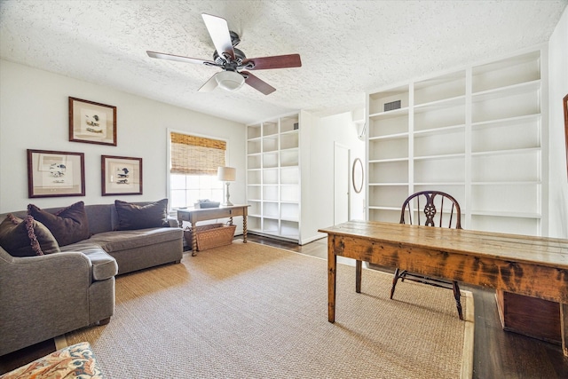 office area with visible vents, built in shelves, wood finished floors, a textured ceiling, and a ceiling fan