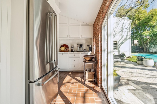 kitchen featuring backsplash, white cabinetry, freestanding refrigerator, and brick floor